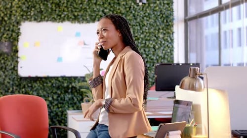 Happy african american casual businesswoman talking on smartphone in office