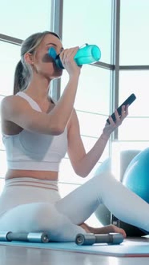 Woman Drinks Water and Uses Phone After Workout