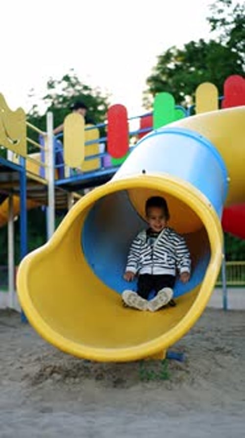 Happy smiling baby appears from the tunnel slide. Caucasian kid having fun time at the playground.