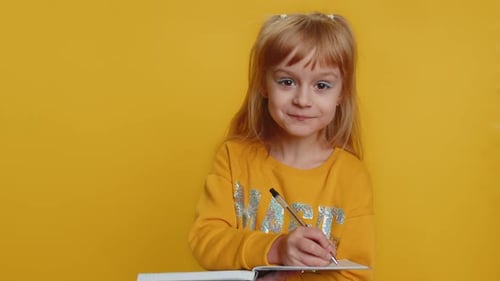 Child Writes in Notebook on Yellow Background