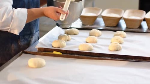 Afroamerikanische Frau in Schürze kippt Schüssel und bürstet Brötchen zum Backen in der Bäckerei, Kopierraum
