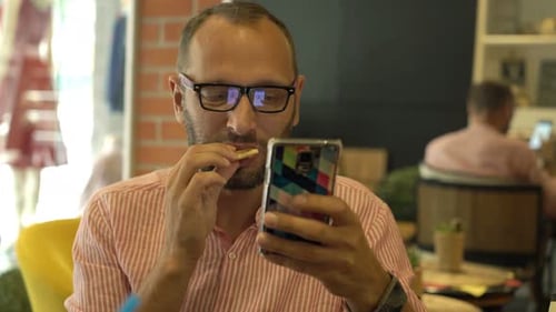 Young Man with Smartphone Eating Sandwich in Cafe 30s