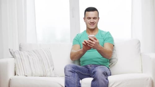 Home, Technology and Internet Concept - Smiling Man with Smartphone Sitting On
