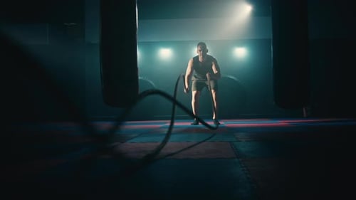 Athletic Man Exercising with Battle Ropes in Gym