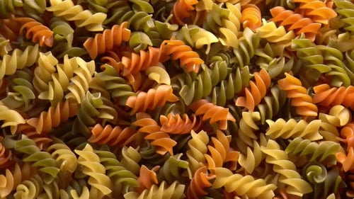 Pâtes italiennes multicolores Fusilli ou Rotini, fond rotatif, gros plan, lumière du soleil, vue du dessus. blé dur