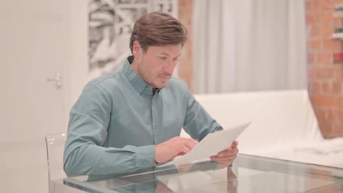 Man Studying Document While Sitting at Table Indoors