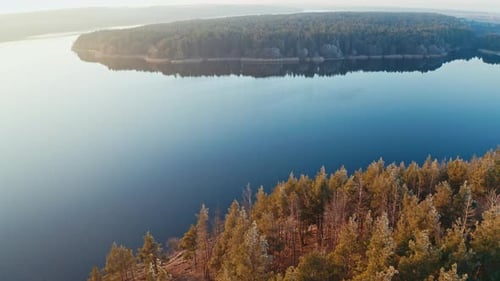 Beautiful panorama of a blue river in nature. Calm lake surrounded by thick forests at sunset.
