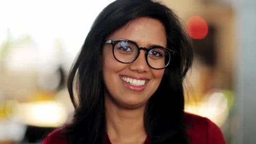 Woman Smiling and Adjusting Glasses in Office Setting