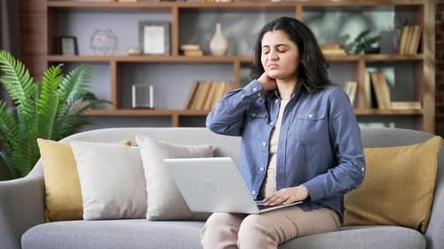 Young Woman Massaging Stiff Neck While Using Laptop