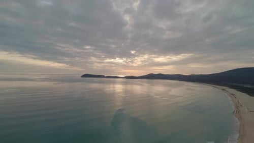 Aerial View of Beach with Calm Transparent Sea Water and Sky Reflection at Sunset Camera Moves