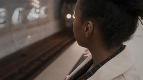 Schwarze Frau steht neben der U-Bahn mit vorbeifahrendem Zug