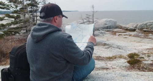 Adult Man Reading Map on Rocky Coastal Landscape