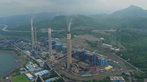 Aerial view of a large coal fired power plant with tall smokestacks releasing smoke into the