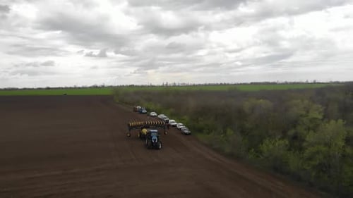 Blue tractor planting sunflower with yellow planter on the field in Ukraine