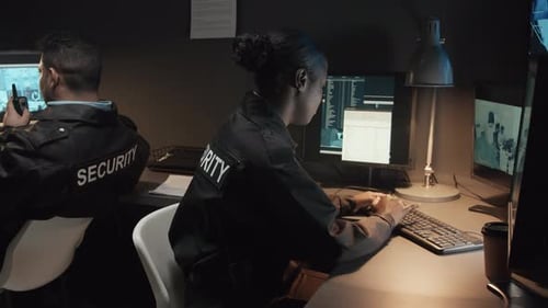 Security Guards Monitoring Surveillance Screens in Dark Office