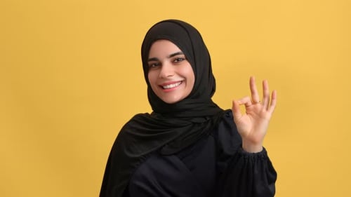 Happy Beautiful Turkish Woman in Black Hijab Showing Ok Okay Cool Gesture Posing Isolated on Orange
