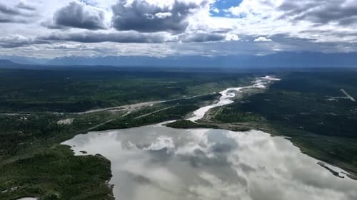 Riesiges grünes Tal, das vom Fluss durchquert wird. Graue Wolkenlandschaft spiegelt sich in der Wasserlandschaft
wider.