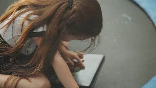 Child Sitting on a Trampoline and Looking at a Tablet