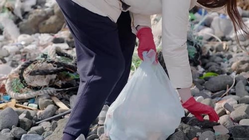 Woman Picks Up Trash on Rocky Beach