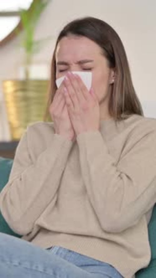 Kranke junge Frau niest auf dem Sofa, vertikales Video