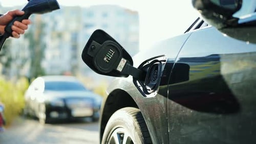 Businessman Charges Sleek Electric Vehicle On a Sunny Street Green Technology