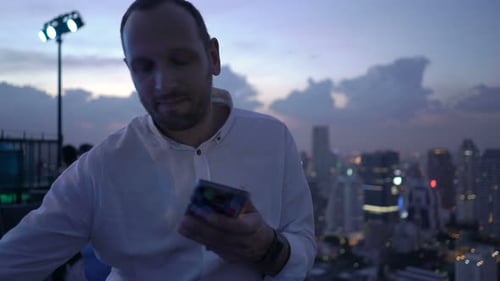 Young Man with Smartphone Drinking Cocktail Standing on Terrace in Bar Alcohol
