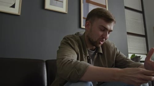 Man Sits on Couch and Talks Indoors