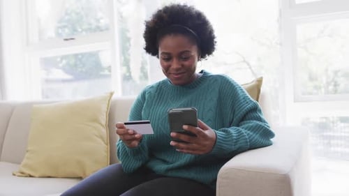 Woman Uses Phone with Credit Card on Sofa