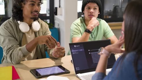 Groupe d'étude diversifié discutant du projet après un message de discussion apparaissant sur un ordinateur portable dans une zone d'étude partagée