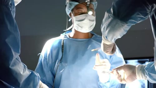 Diverse surgeons wearing surgical gowns operating on patient in operating theatre, slow motion