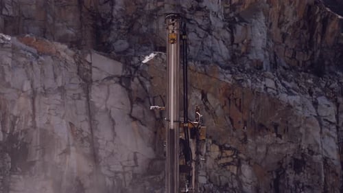 Vertical drilling rig piercing through the rock face of a stark quarry cliff