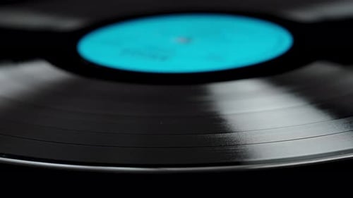 Close-up of a vinyl record with a blue label slowly rotating on a black background.