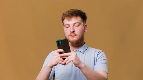 A Teenage Guy with Red Hair Looks Intently at His Mobile Phone While Sitting in a Studio Shot