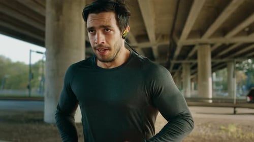 Athletic Young Man in Earphones and Sports Outfit is Jogging in the Street. He is Running in an Urb