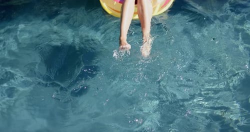 As pernas de uma adolescente são visíveis, penduradas na água azul clara da piscina em um carro alegórico amarelo com um policial