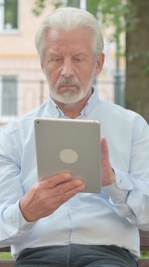 Senior Old Man using Tablet while Sitting in Park, vertical video