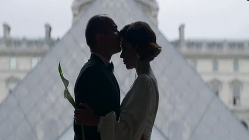 Casal feliz perto da pirâmide do museu do Louvre em Paris. Ação. Vista lateral do abraço da noiva e do noivo