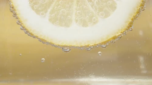 Lemon slice, bubbles in Lemonade. Honey flows down it. Close-up Slow motion.