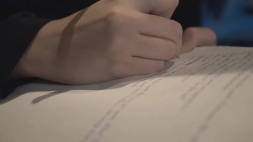 A Person In Blue Sweater Writing In Small Letters On A White Paper. -closeup shot
