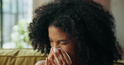 Woman, sneeze and tissue on sofa in home, sick and sinusitis with flu, allergy