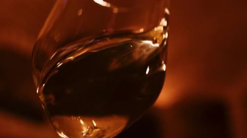 Connoisseur swirling white wine in wine glass; slow motion close-up