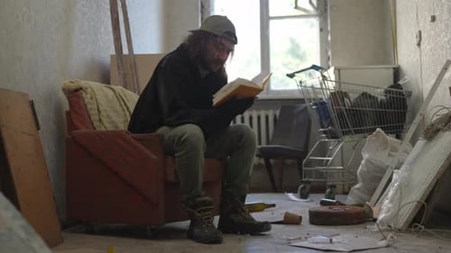 Pobre hombre sin hogar sentado en una habitación de un edificio abandonado lleno de sus escasas pertenencias Él es