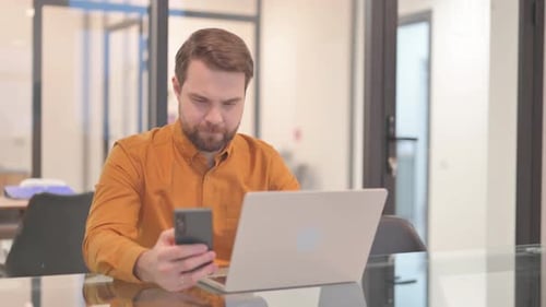 Young Adult Working at Desk With Laptop and Cellphone