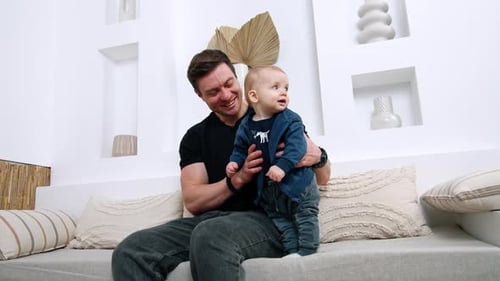 Man Holds Smiling Baby on Lap on Couch