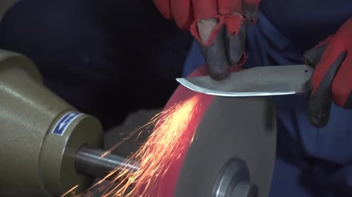 Gloved Worker Sharpening a Knife on Grinding Wheel