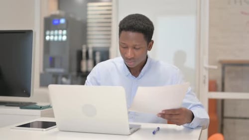 Young Adult Working at Desk with Laptop and Paperwork