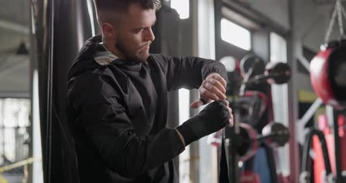 Un joven con un chándal oscuro se envuelve las manos con vendajes antes de un combate de boxeo u otro