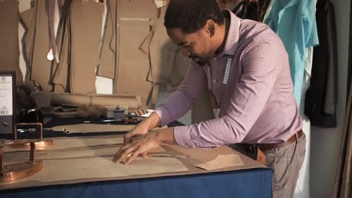 Male fashion tailor working on the measurements for the suit design in his workshop.