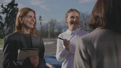 Four Beautiful Young Business Women are Standing Near a Car on the Street and Discussing a Business