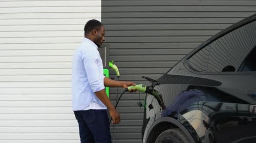 African American Man Disconnects Power Connector Into Luxury EV Car at Station
